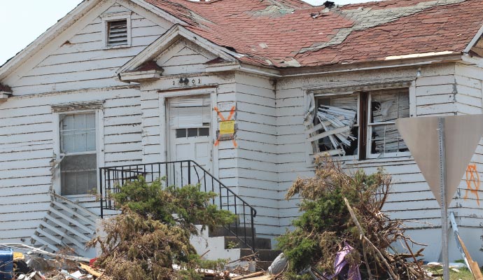 A storm-damaged residential home with broken windows and roof