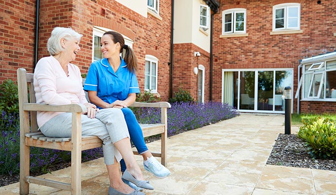 An elderly woman and a caregiver sitting on a wooden bench