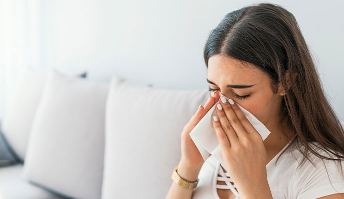 A young woman sneezing into a white tissue