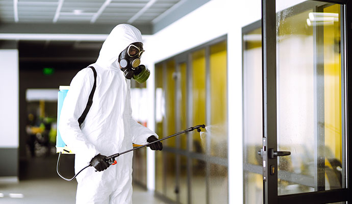 Professional using a pressurized sprayer to sanitize glass doors in a modern office