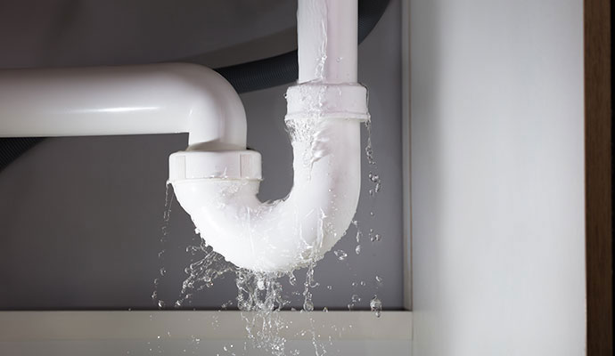 Water dripping from a white PVC P-trap pipe under a kitchen sink