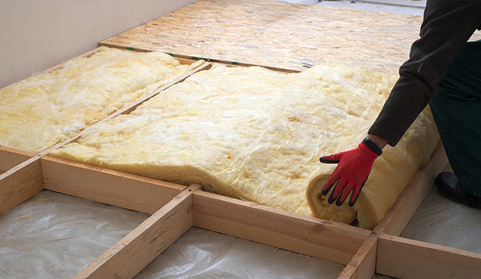 A professional installing fiberglass insulation between wooden floor joists
