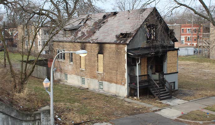 Fire-damaged residential house with boarded-up windows and damaged roof