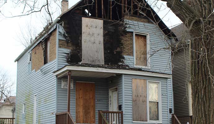 Plywood board-up coverings secured over windows and door on a fire-damaged house