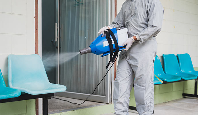 A professional with hazmat suits sanitizing commercial space with equipment
