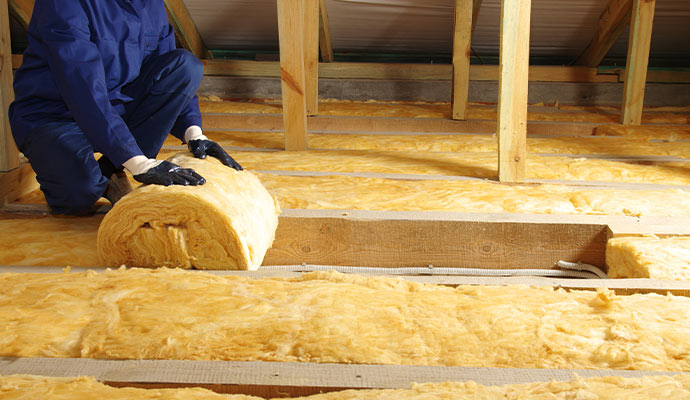 Technician installing fiberglass insulation in an attic.