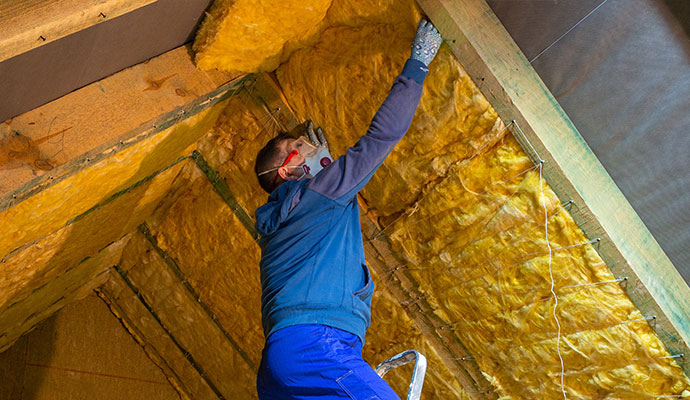 Worker installing yellow fiberglass insulation between roof rafters