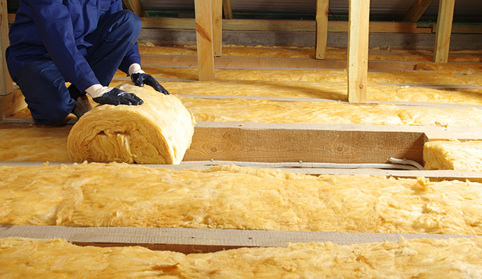 Worker installing yellow fiberglass insulation in attic