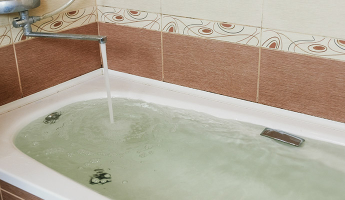 Faucet running water overflowing bathtub in bathroom