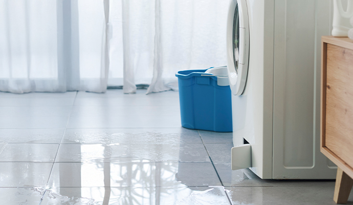Leaking washing machine with water puddle on tiled floor
